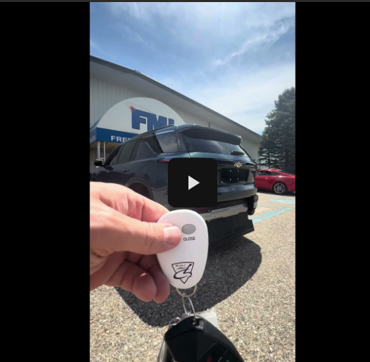Hand holding a car key fob in front of a black SUV with a building in the background
