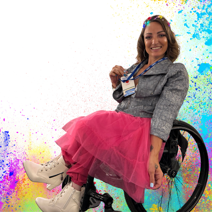 Woman in a wheelchair wearing a pink skirt and gray jacket against a colorful abstract background