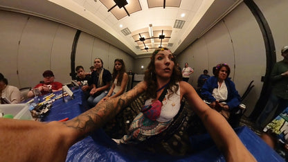 Woman that is teaching art in a room with people and tables.